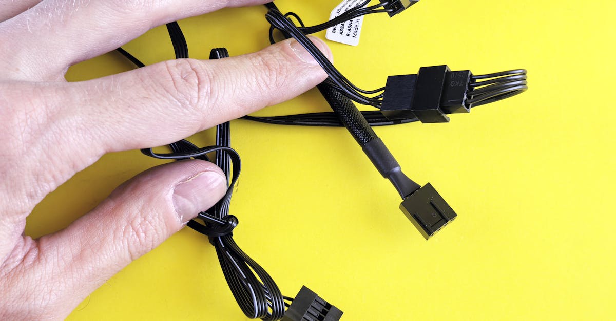 a hand holding black computer cables against a bright yellow background showcasing technology conne